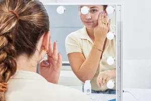 Person looking into a mirror applying EltaMD AM Therapy Face Moisturizer on their face