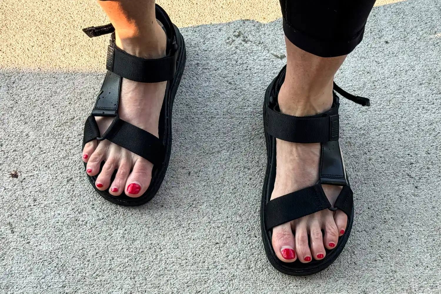 Feet wearing the FitFlop Women's GEN-FF Adjustable Webbing/Leather Back-Strap Sandals on concrete