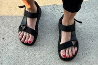 Feet wearing the FitFlop Women's GEN-FF Adjustable Webbing/Leather Back-Strap Sandals on concrete