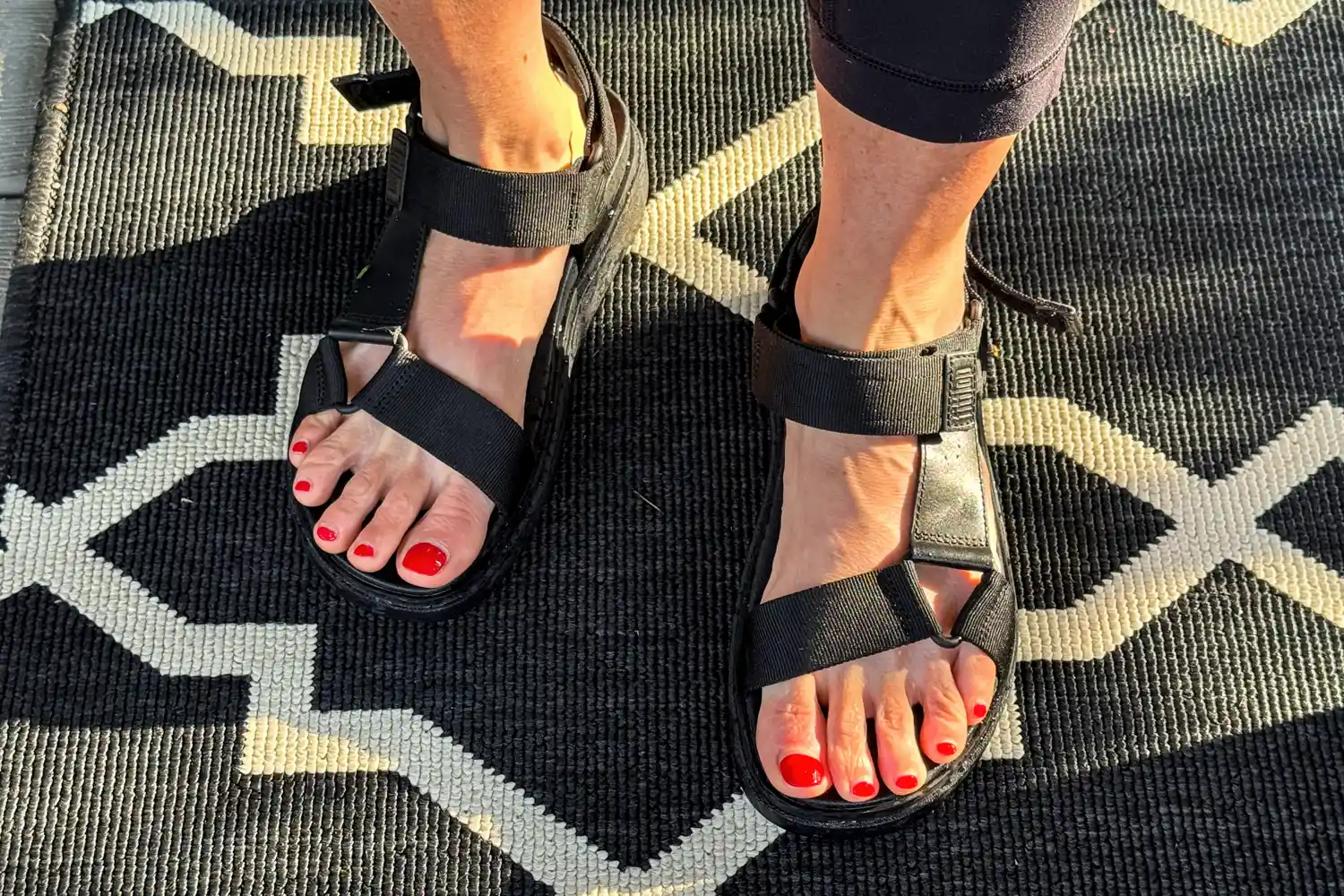 A person wearing FitFlop Women's GEN-FF Adjustable Webbing/Leather Back-Strap Sandals standing on a patterned rug