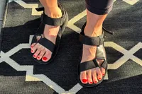 A person wearing FitFlop Women's GEN-FF Adjustable Webbing/Leather Back-Strap Sandals standing on a patterned rug