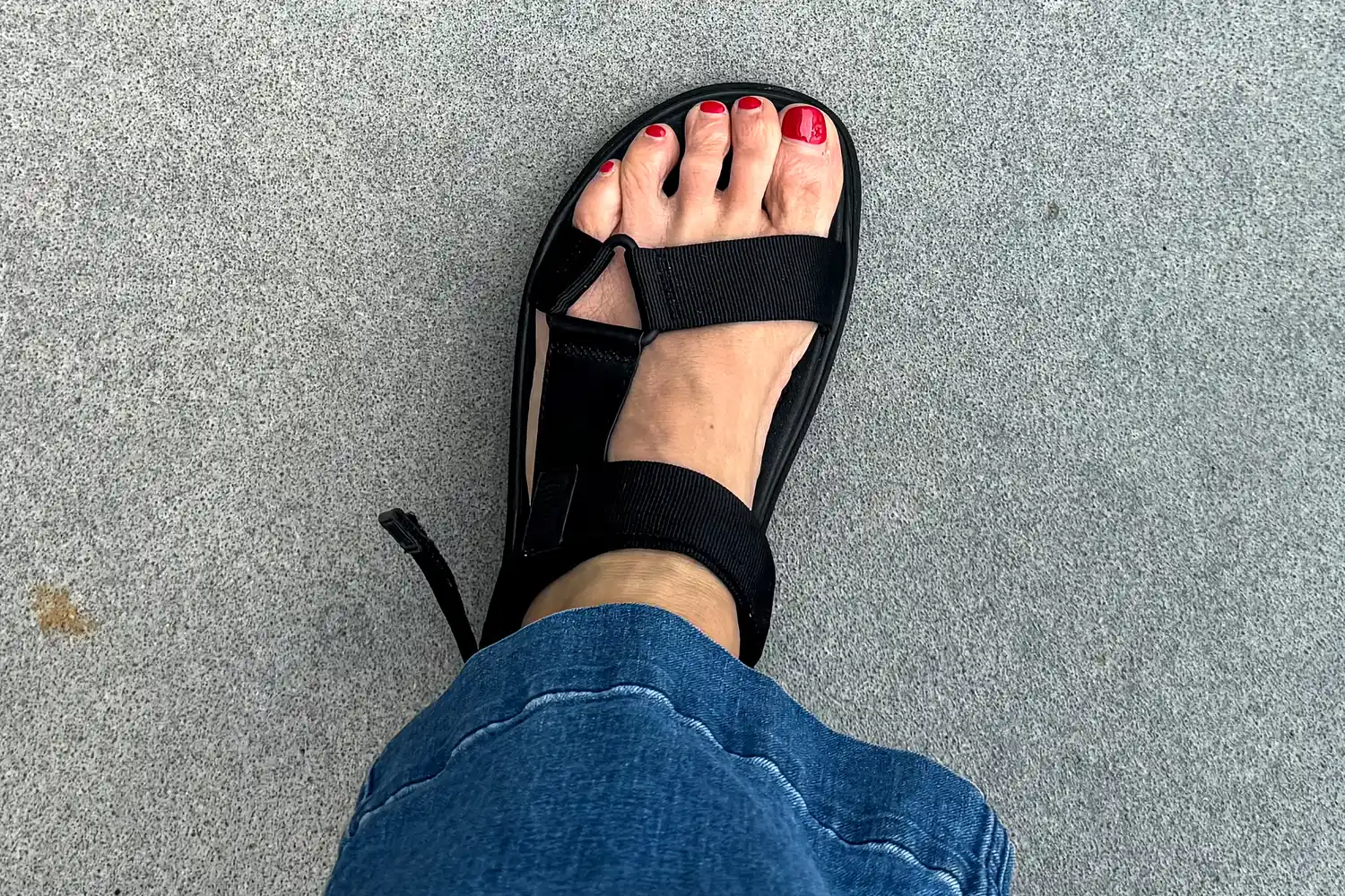 A person's foot wearing the FitFlop Women's GEN-FF Adjustable Webbing/Leather Back-Strap Sandal with jeans