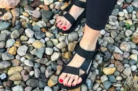 A person wearing FitFlop Women's GEN-FF Adjustable Webbing/Leather Back-Strap Sandals standing on a rocky surface