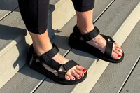 Feet wearing FitFlop Women's GEN-FF Adjustable Webbing/Leather Back-Strap Sandals on a wooden staircase