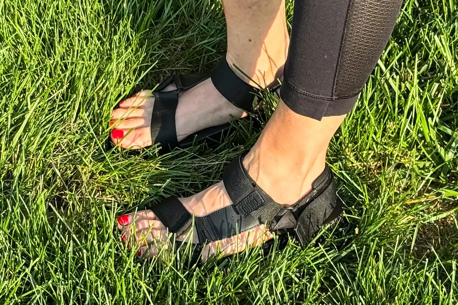 A person wearing FitFlop Women's GEN-FF Adjustable Webbing/Leather Back-Strap Sandals standing on grass