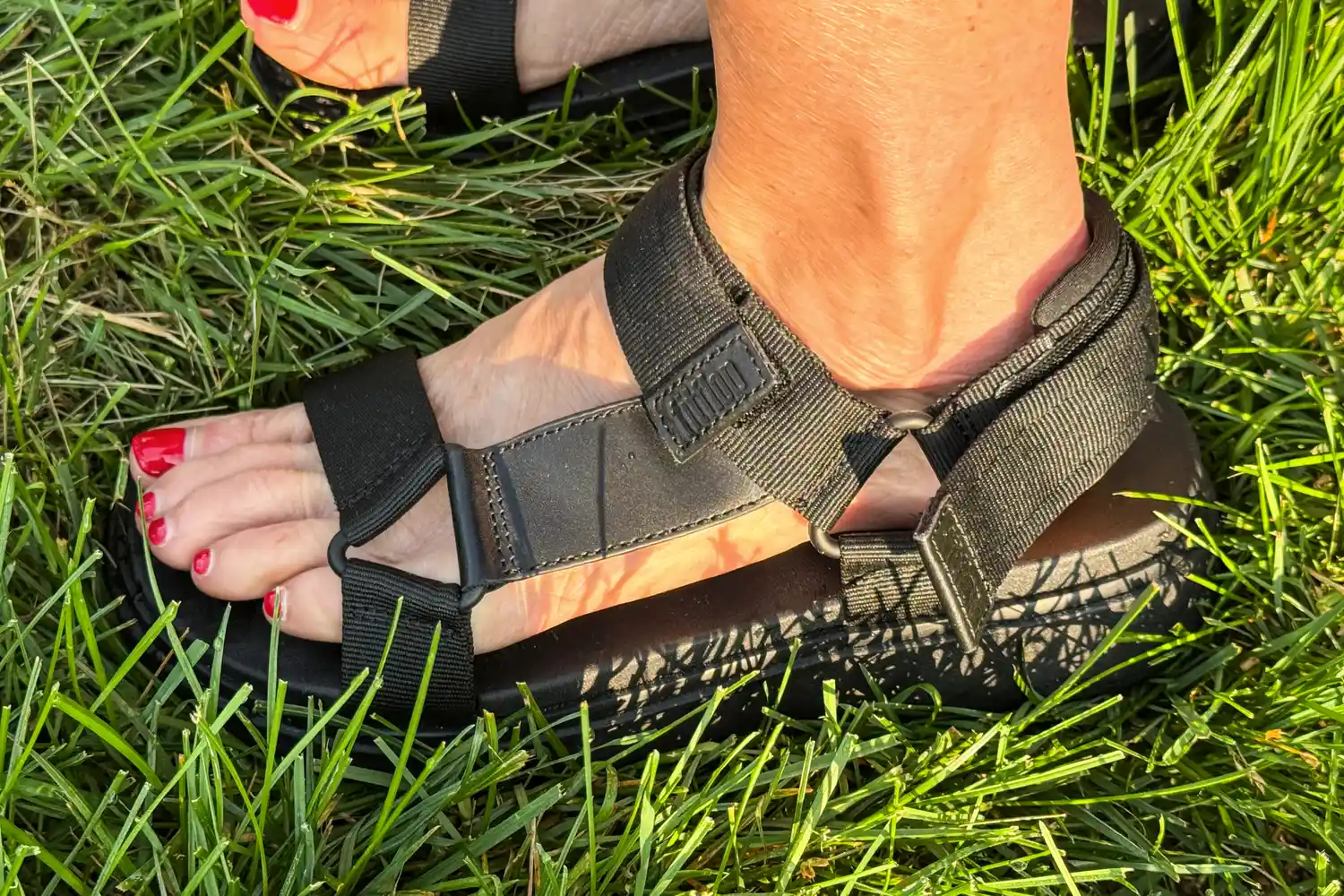 A side view of a person wearing FitFlop Women's GEN-FF Adjustable Webbing/Leather Back-Strap Sandals standing on grass