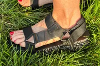 A side view of a person wearing FitFlop Women's GEN-FF Adjustable Webbing/Leather Back-Strap Sandals standing on grass