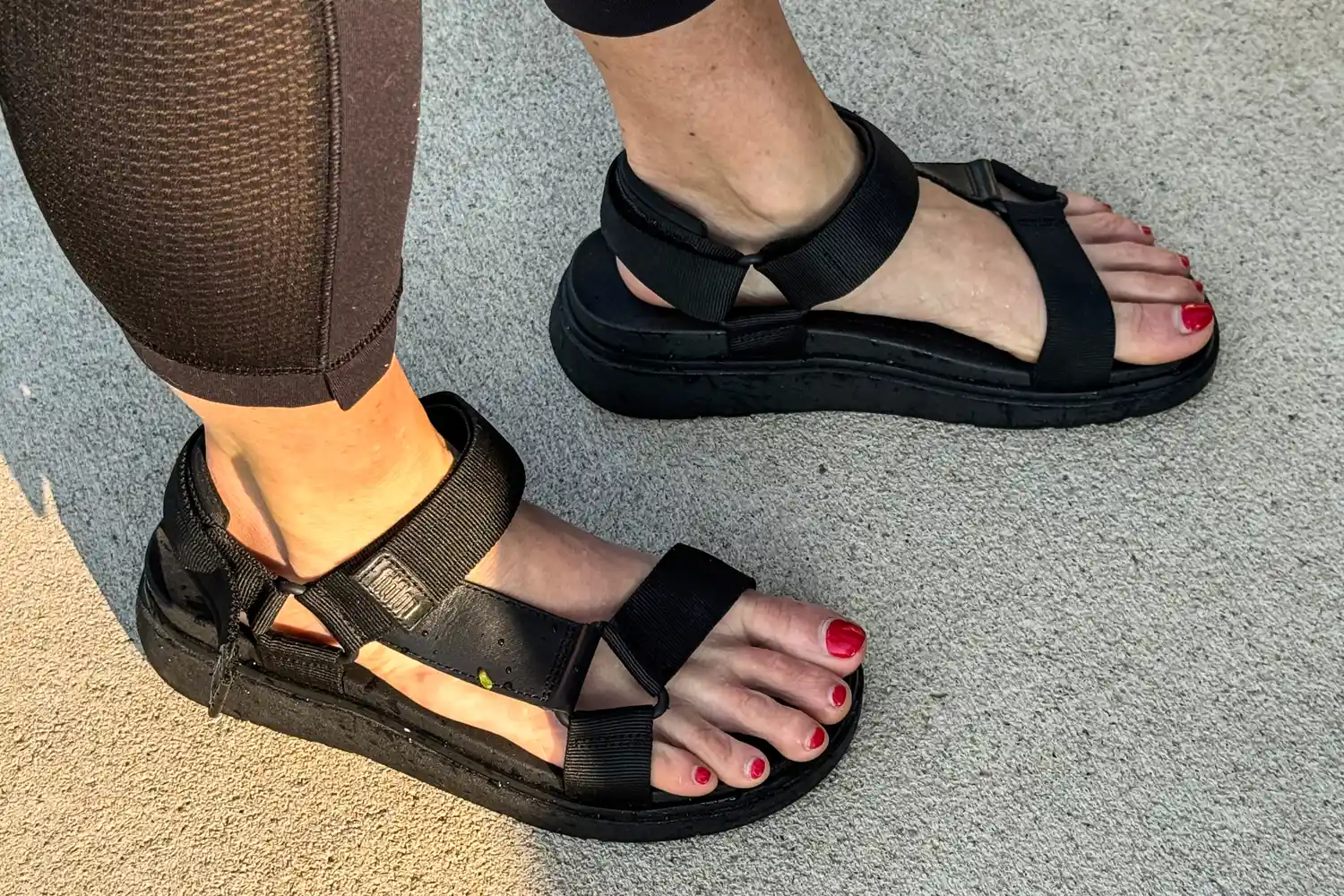 A person wears the FitFlop Women's GEN-FF Adjustable Webbing/Leather Back-Strap Sandals with black leggings