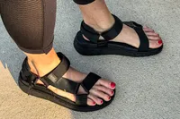 A person wears the FitFlop Women's GEN-FF Adjustable Webbing/Leather Back-Strap Sandals with black leggings