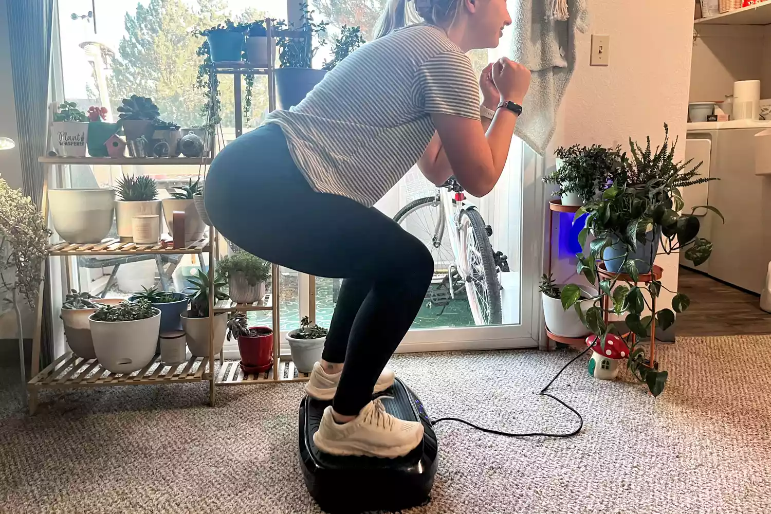 A person squats on top of the Flybird Mini Vibration Plate