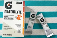 Gatorlyte Rapid Rehydration electrolyte powder packaging and two sachets on a striped surface