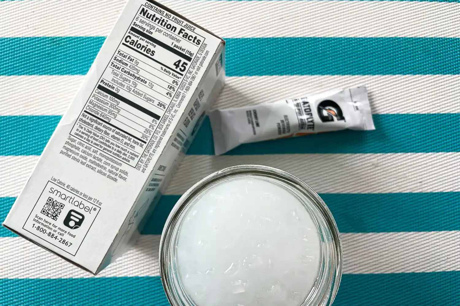Nutrition label on a box a packet and a glass of ice water on a striped surface