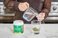 Person pouring water to mix with Amazing Grass Greens Blend Superfood