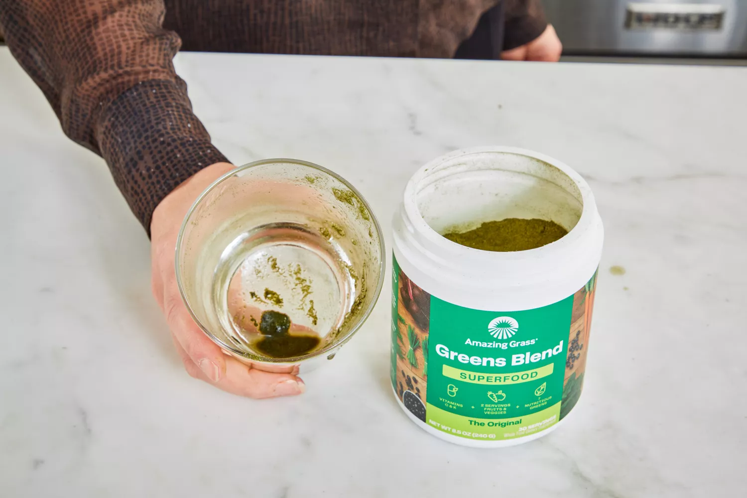 Person holding glass next to open container of Amazing Grass Greens Blend Superfood