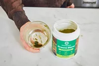 Person holding glass next to open container of Amazing Grass Greens Blend Superfood