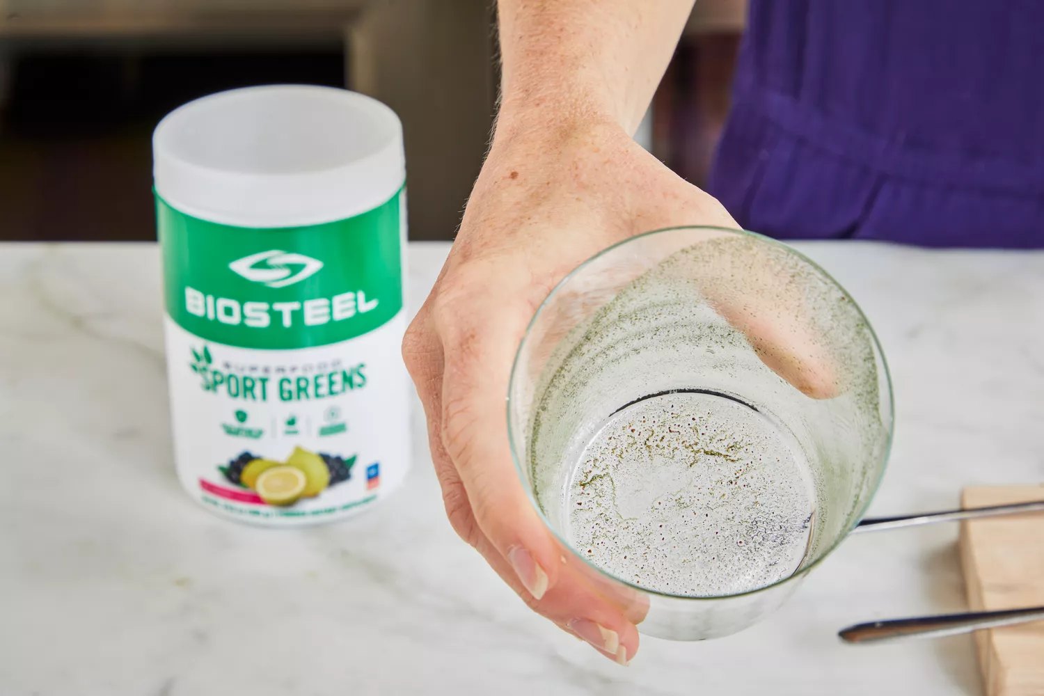 Person holding glass next to BioSteel Powdered Greens Antioxidant Superfood container