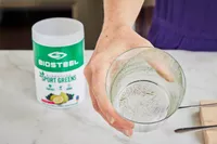 Person holding glass next to BioSteel Powdered Greens Antioxidant Superfood container