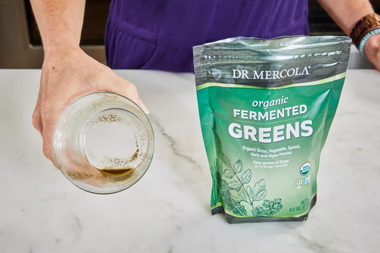Person holding glass next to Dr. Mercola Fermented Greens Powder