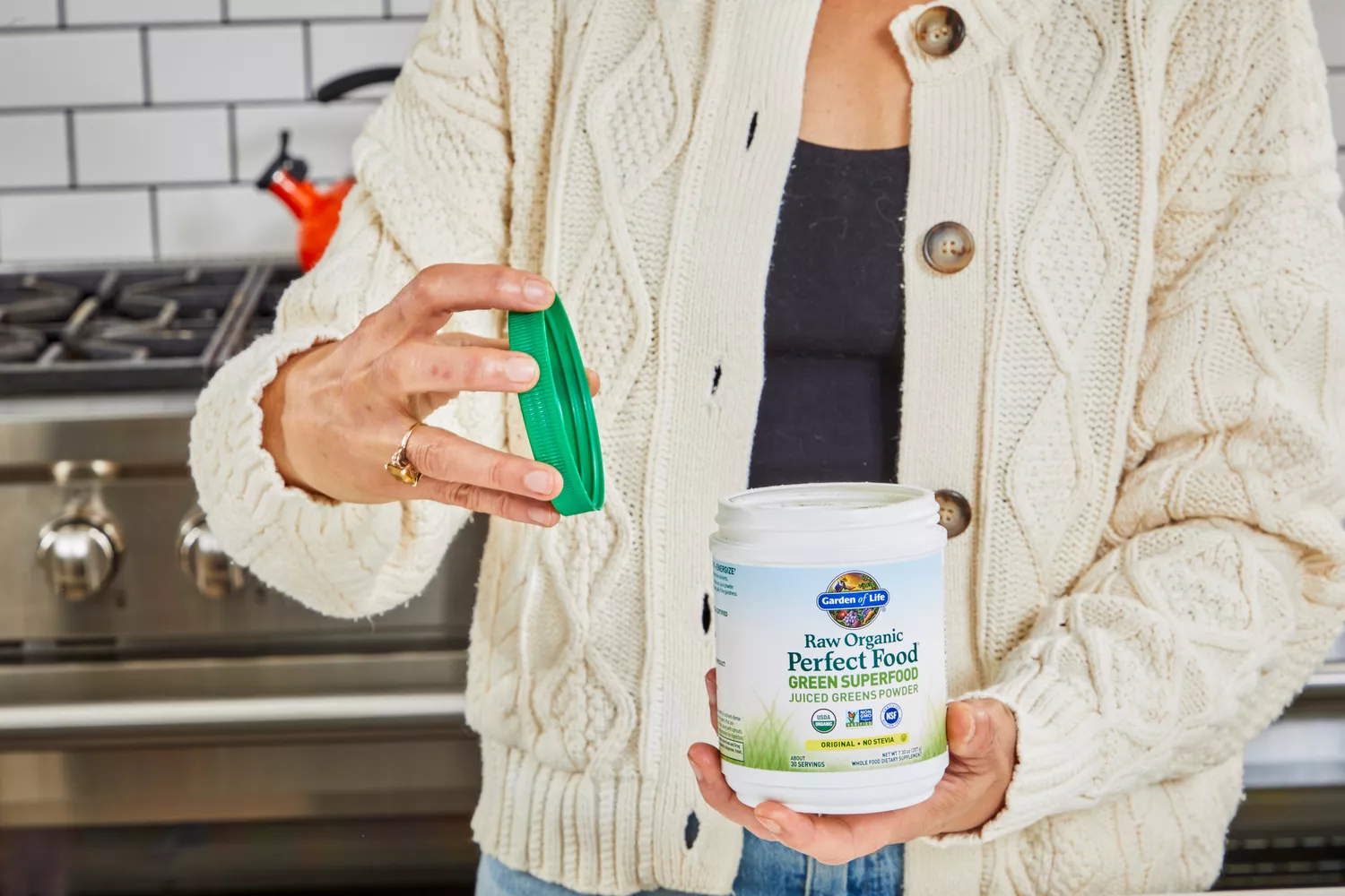 Person holding container of Garden of Life Raw Organic Perfect Food Green Superfood with open lid