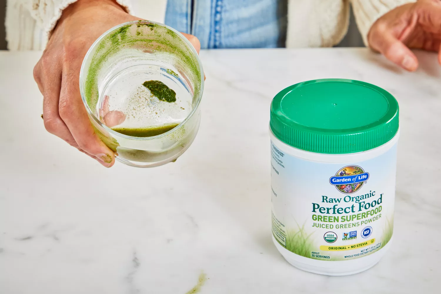 Hand holding glass next to Garden of Life Raw Organic Perfect Food Green Superfood