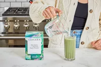 Person pouring water into a glass with Sakara Organic Protein + Greens Super Powder