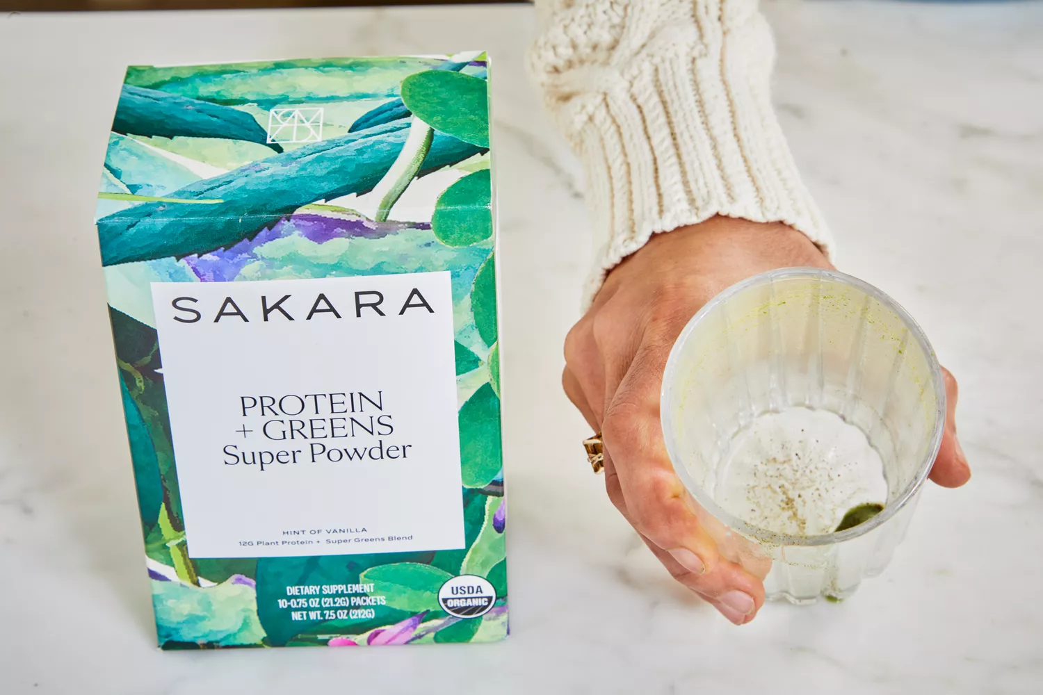 Person holding glass next to Sakara Organic Protein + Greens Super Powder