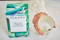 Person holding glass next to Sakara Organic Protein + Greens Super Powder