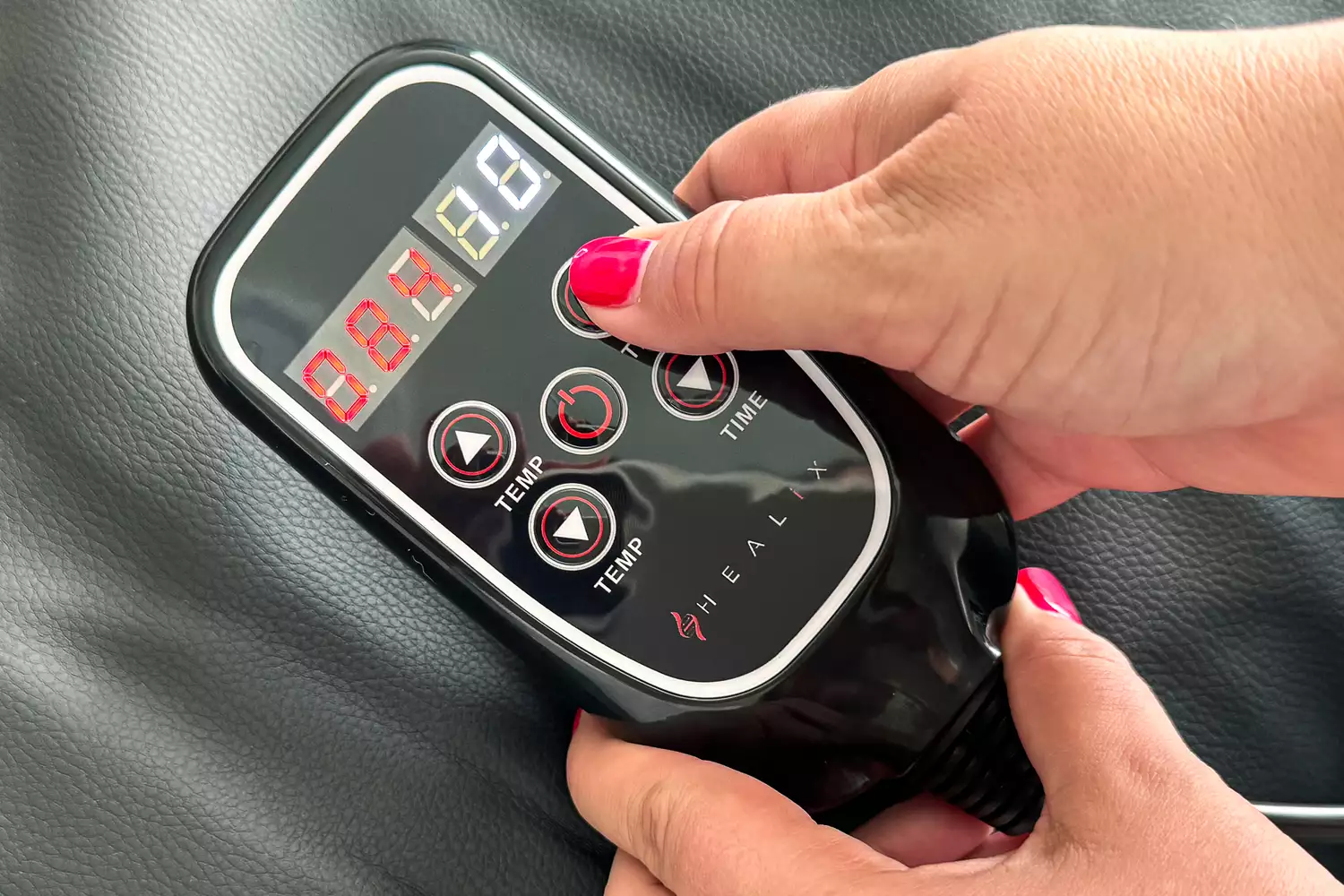 A hand holding the remote to the HEALiX-Z Sauna Blanket