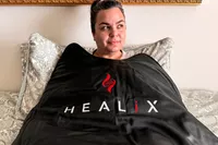 A person inside of the HEALiX-Z Sauna Blanket resting on a bed