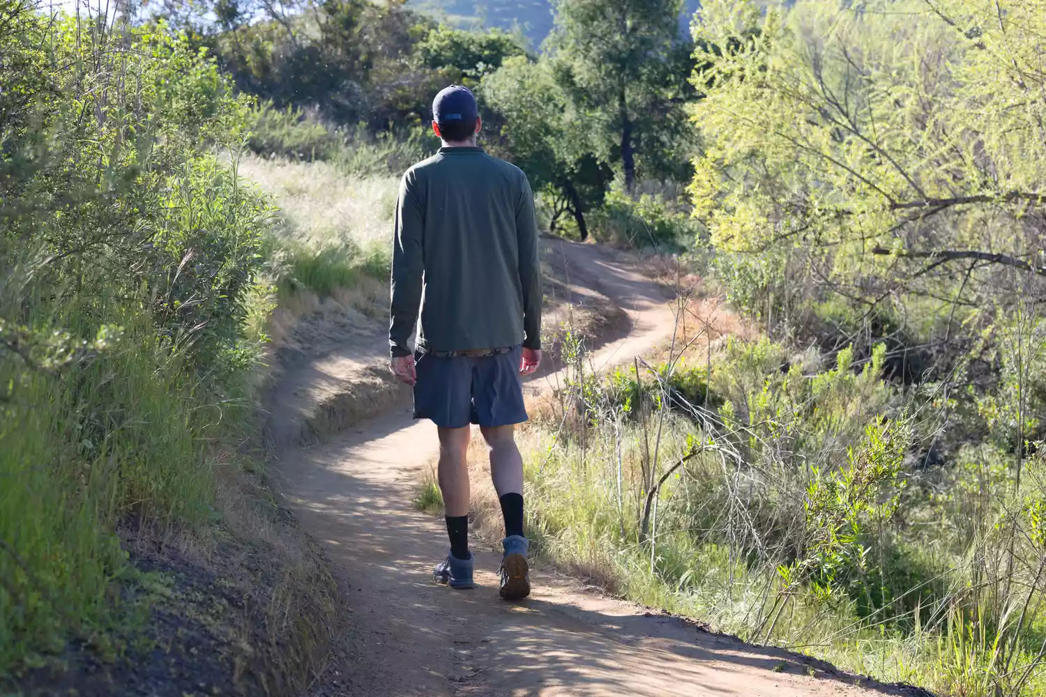 A man walks down a dirt walking path while wearing Arc'teryx Aerios FL 2 Mid GTX Hiking Shoe