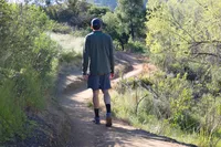A man walks down a dirt walking path while wearing Arc'teryx Aerios FL 2 Mid GTX Hiking Shoe