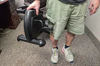 A person lifts the Himaly Mini Exercise Bike by the vertical base
