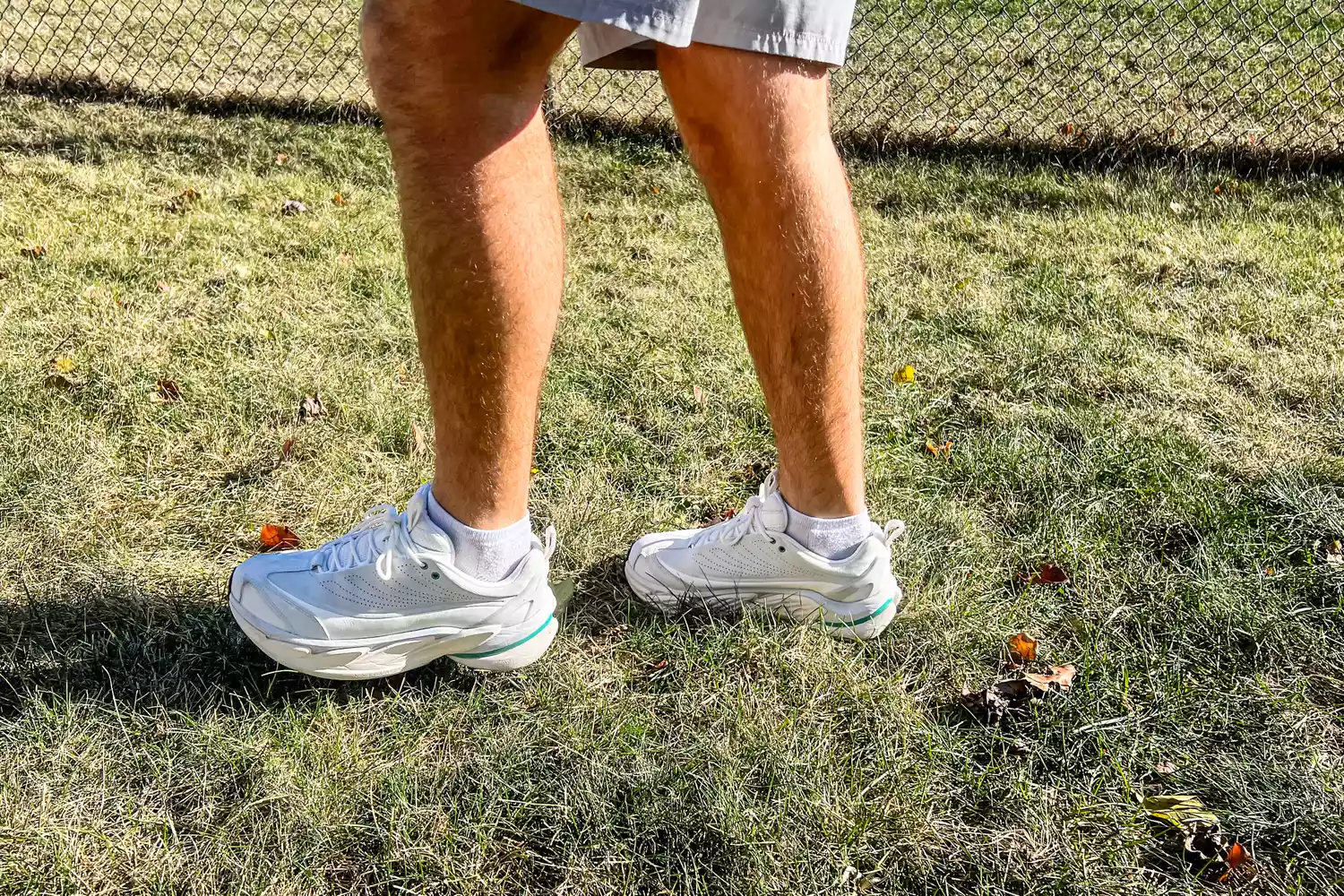A person wears the Hoka All Gender Elevon X Running Shoes while walking through grass