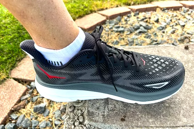 A person walks outside while wearing the Hoka Men's Clifton 9 Running Shoes