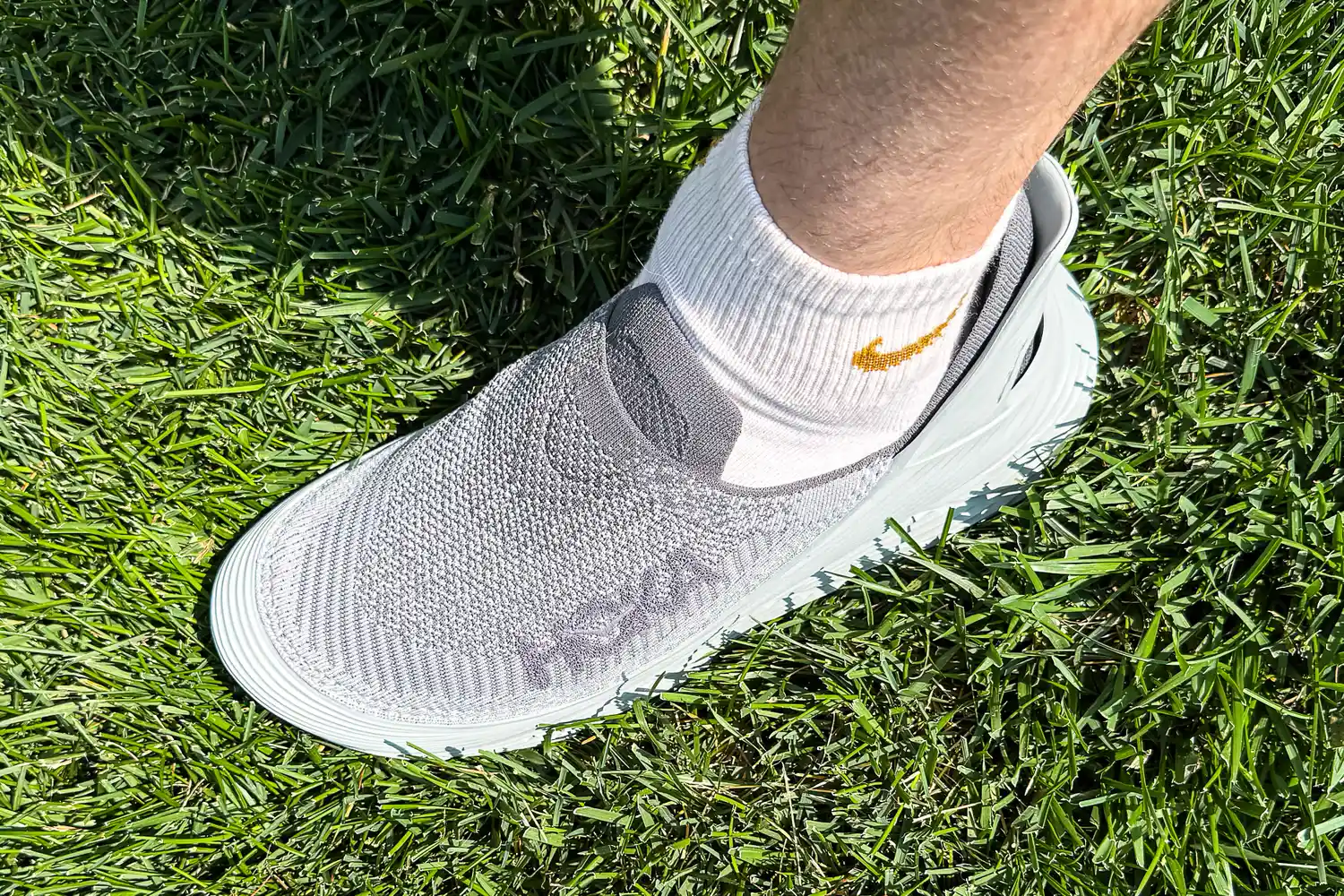 A person wears the Hoka Restore TC Recovery Shoes outside in grass