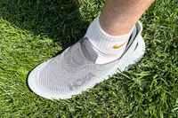 A person wears the Hoka Restore TC Recovery Shoes outside in grass