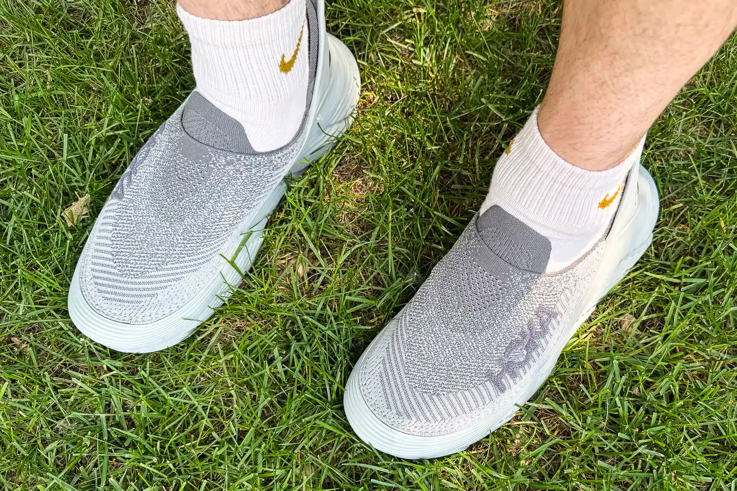 A person wears the Hoka Restore TC Recovery Shoes while standing in grass