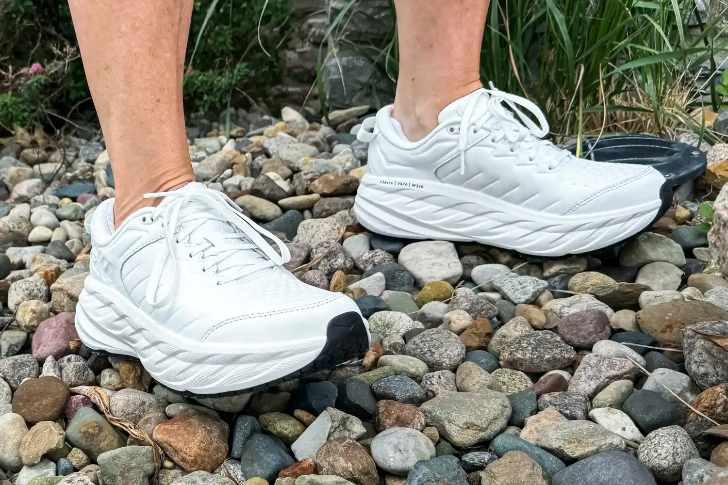 A person walks outside on pebbles while wearing the Hoka Women's Bondi SR Road Shoe