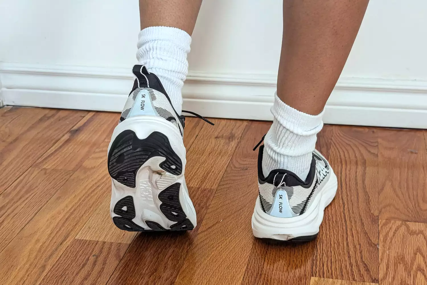 A person's legs posed while wearing the Hoka Women's Skyflows on a wooden floor