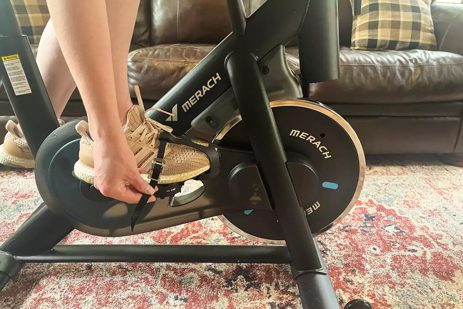 A person secures the pedals of the Merach S26 Exercise Bike to their sneakers