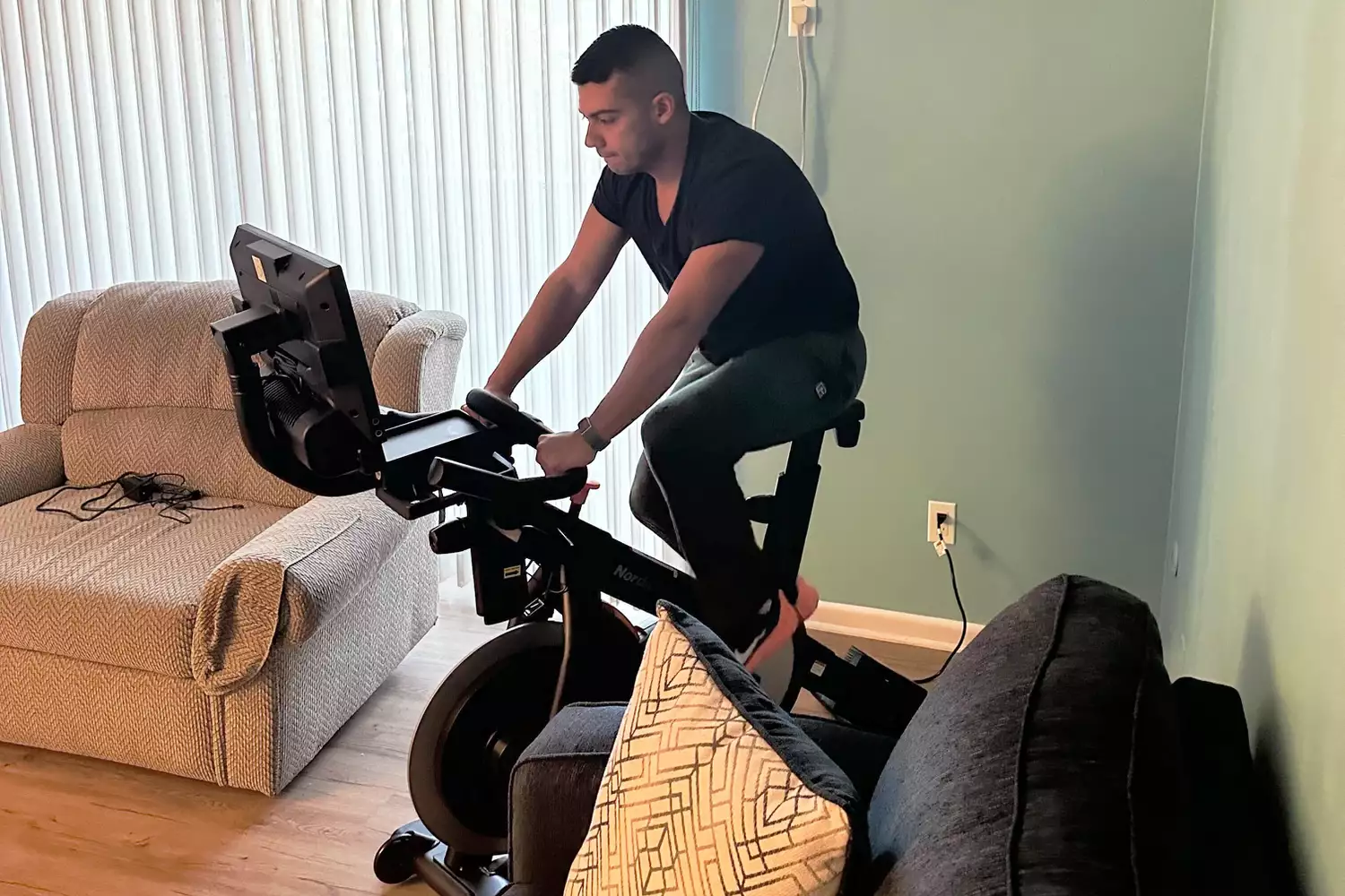 Person riding the NordicTrack Commercial S15i Studio Cycle in between two sofas