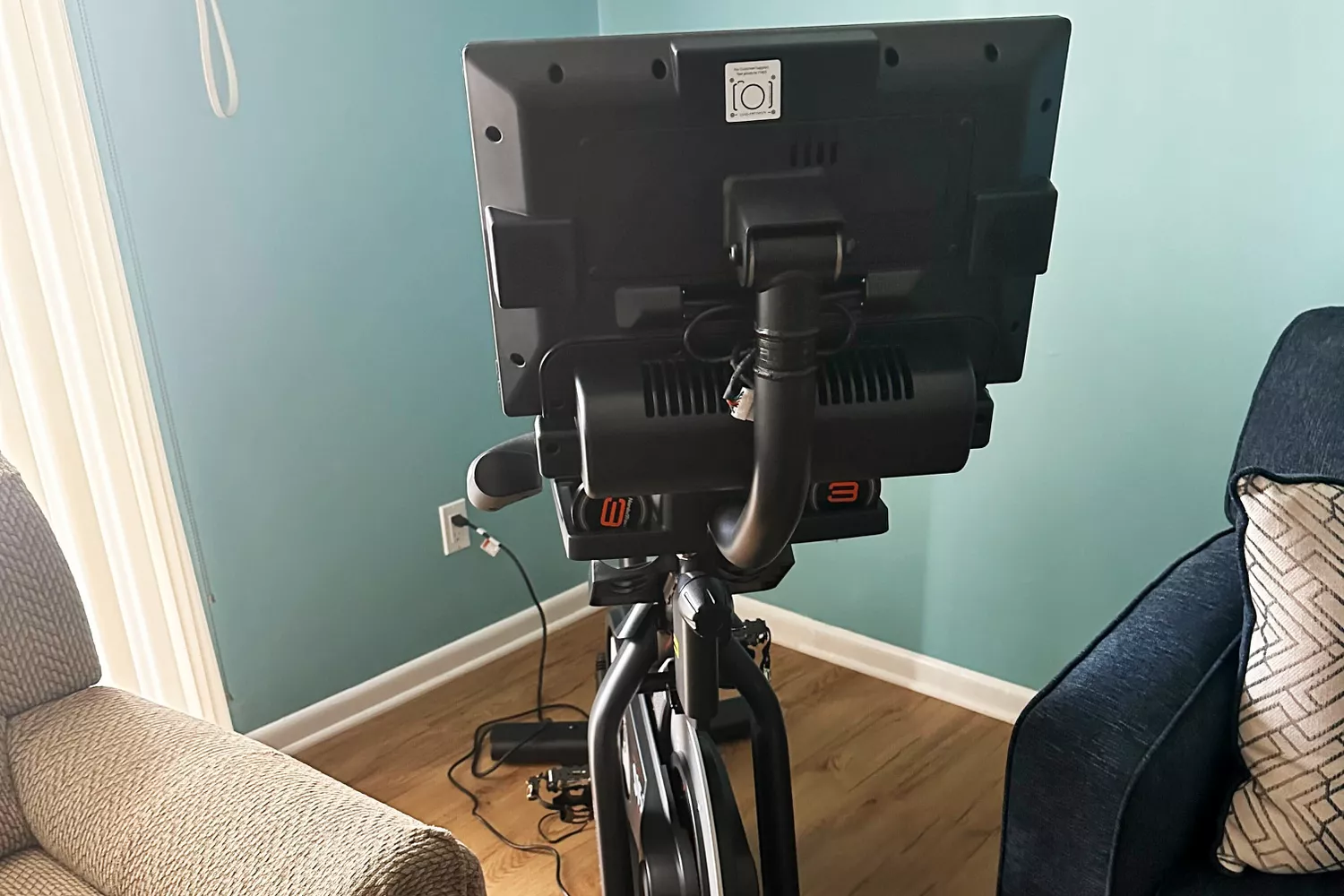 NordicTrack Commercial S15i Studio Cycle set up on a wood floor in between two sofas