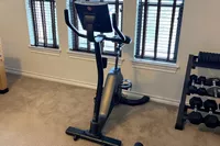 Schwinn Upright Bike Series set up on a carpet next to a window and a set of weights