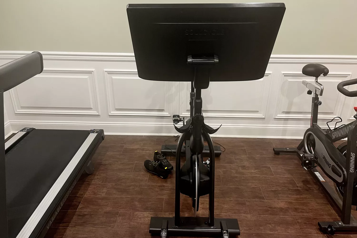 Equinox+ SoulCycle At-Home Bike on hardwood floor between treadmill and another stationary bike