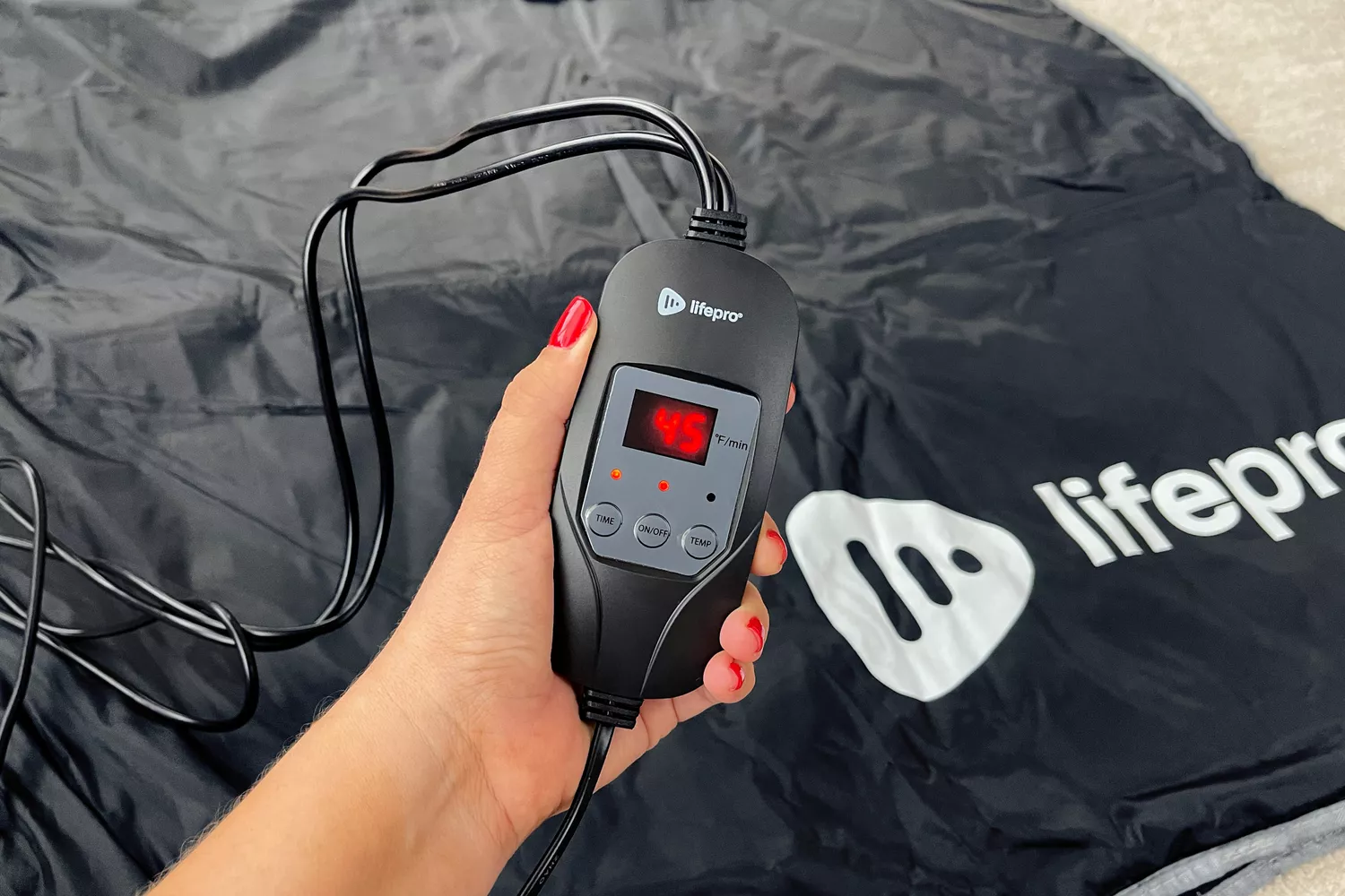 A person holds the control panel for the LifePro BioRemedy Infrared Sauna Blanket
