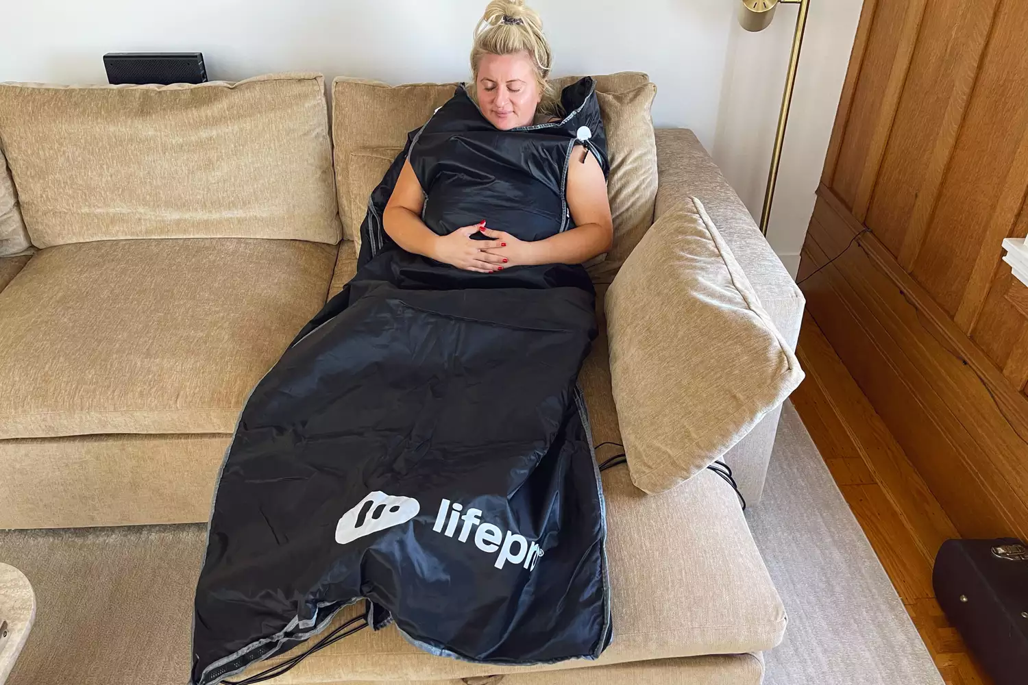 person sitting on couch wearing the LifePro BioRemedy Infrared Sauna Blanket