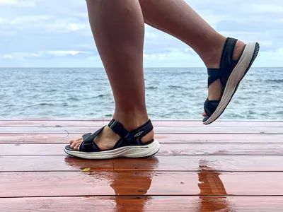 Two legs posed to the side while wearing the Keen Women's Leiki Open-Toe Sandals on a dock