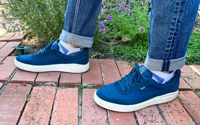 A person wears the Kizik Men's Prague 2 Sneakers while walking on brick outside