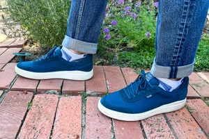 A person wears the Kizik Men's Prague 2 Sneakers while walking on brick outside