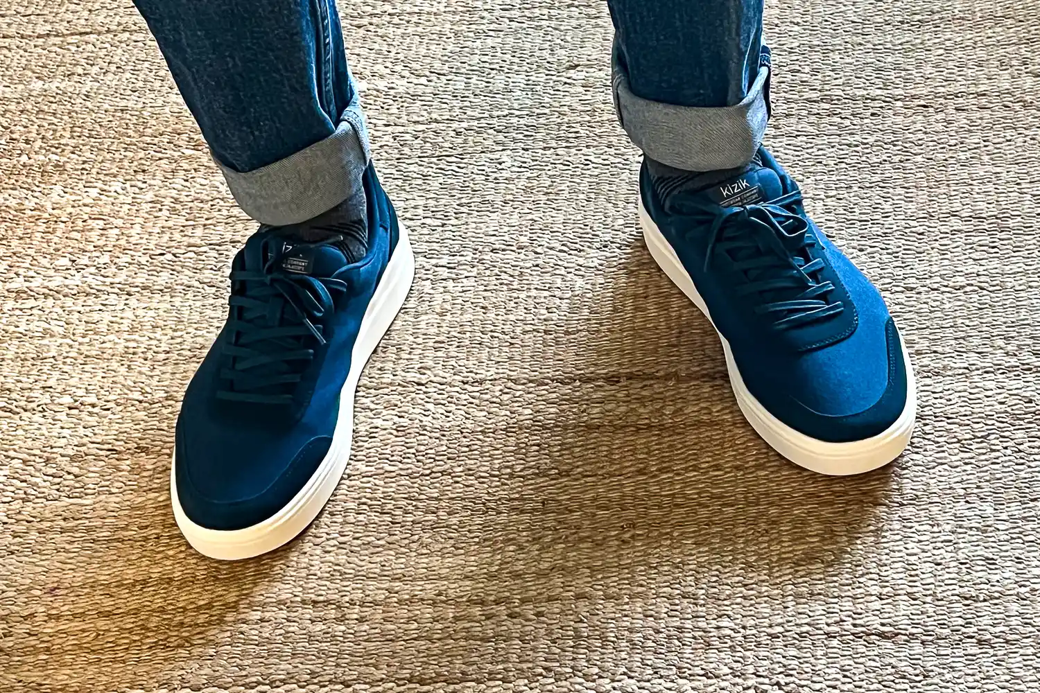 A person wears the Kizik Men's Prague 2 Sneakers on a jute rug